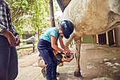 Girl cleaning horse hoof outside stables