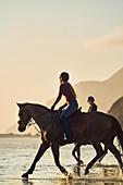 Young woman horseback riding on ocean beach at sunset