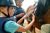 Girls adjust stirrups preparing for horseback riding