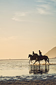 Young women horseback riding in ocean surf