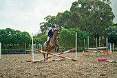 Teenage girl equestrian jumping in paddock