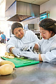 Women with Down Syndrome cutting potatoes in cafe kitchen