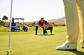 Male golfers planning putt on sunny golf greens