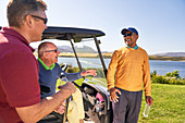 Male golfer friends talking and laughing at golf cart