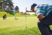 Male golfer preparing to putt on sunny golf course