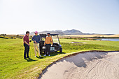 Male golfer friends talking at sand trap