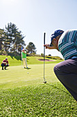 Male golfer preparing to take shot on sunny putting green