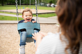 Mother pushing cute toddler girl in swing at playground