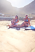 Young female surfer friends relaxing on sunny beach