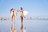 Happy female surfer friends high fiving on sunny beach