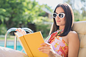 Woman in sunglasses reading book at summer poolside