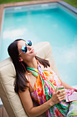Woman with headphones and cocktail at poolside