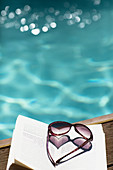 Heart-shape sunglasses on book at summer poolside