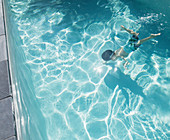 Boy swimming underwater in sunny, summer swimming pool