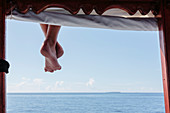 Bare feet hanging from dock over ocean, Maldives