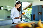 Woman drinking juice and eating fruit in kitchen