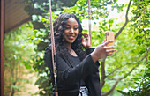 Woman with camera phone posing for selfie on patio swing