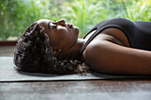 Serene woman laying in corpse pose on yoga mat