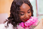 Close up serene woman smelling fresh pink peony flowers