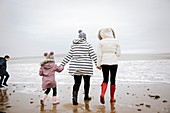 Family in warm clothing walking on winter ocean beach