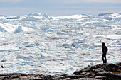 Man on rocks looking at glacier ice melt view Greenland