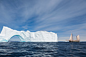 Ship sailing toward majestic iceberg with arch Greenland