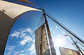 Wooden and mast and sailboat sails below blue sky