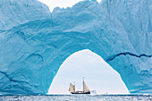 Ship sailing behind majestic iceberg arch