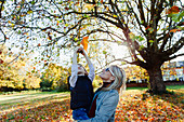 Mother lifting son reaching for autumn leaf in park
