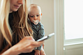Baby girl with pacifier watching mother using smart phone