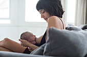 Mother breastfeeding newborn baby on sofa