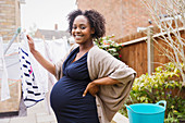 Portrait pregnant woman hanging clothes on clothesline