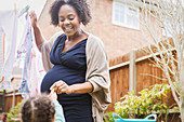Happy pregnant woman hanging clothes on clothesline