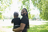 Father with long braids holding toddler son in park