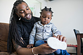 Father with long braids putting shoes on toddler son