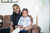 Father with long braids putting shoes on toddler son