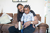 Father putting shoes on toddler son on sofa