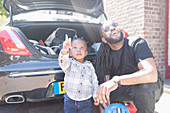 Father and curious toddler son looking up behind car