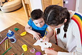 Girl helping brother with Down Syndrome colour at table