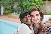 Portrait happy multiethnic couple hugging at poolside