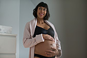 Happy pregnant woman in bathrobe and bra holding stomach