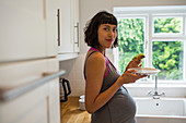 Confident pregnant woman eating avocado toast in kitchen