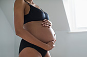 Pregnant woman in bra and panties holding stomach