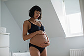 Serene pregnant woman in bra and panties holding stomach