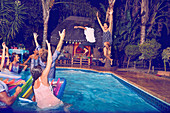 Young friends playing, jumping into swimming pool at night