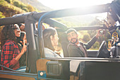 Man with digital camera taking selfie in jeep with friends