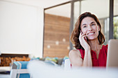 Smiling brunette woman talking on cell phone at laptop