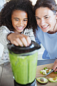 Mother and daughter making healthy green smoothie in blender
