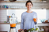 Smiling woman drinking healthy carrot juice in kitchen
