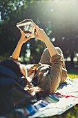 Young woman relaxing and using digital tablet in sunny park